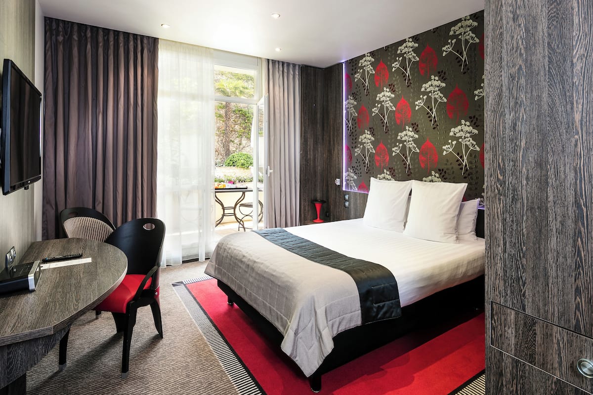 A hotel room with a bed, a desk, a chair, and a TV.