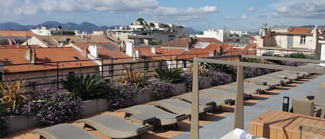 A rooftop terrace with lounge chairs, a wooden table, and potted plants.