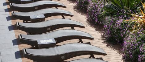 A row of sun loungers with a table in front of a flower bed.