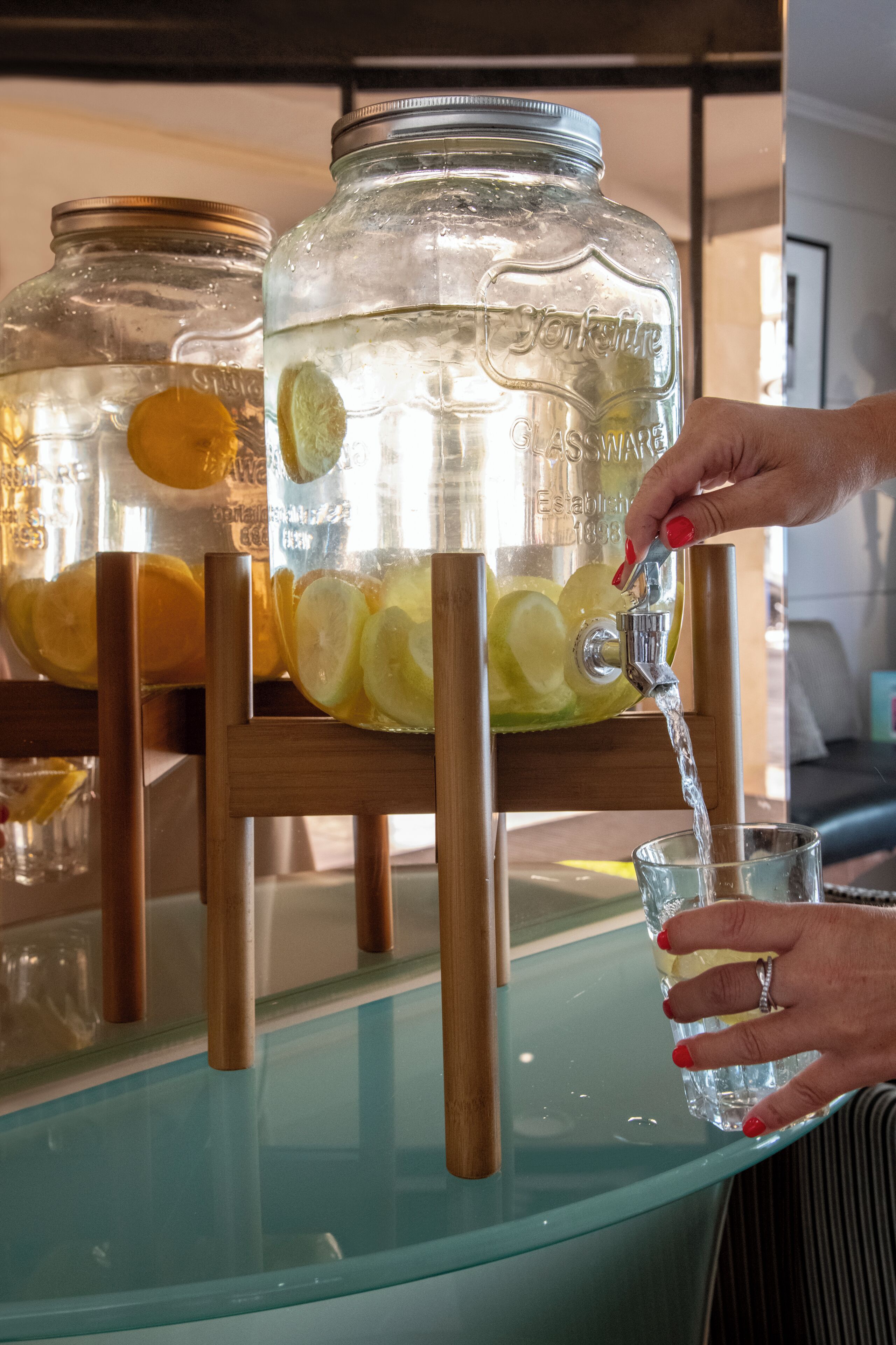 A person pouring water from a glass jar into a glass.