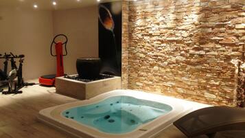 A spa area with a stone wall, a hot tub, exercise equipment, and a massage chair.