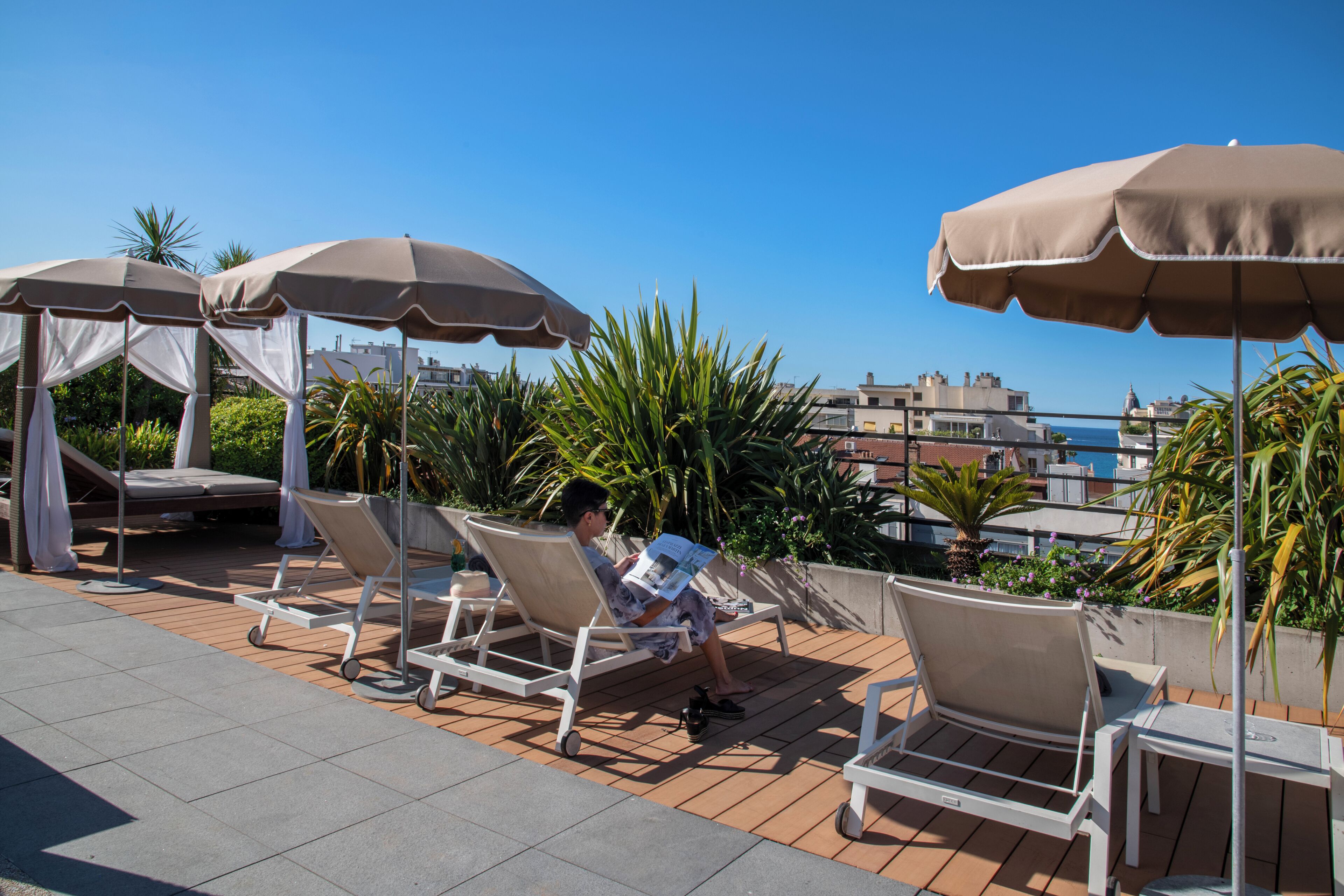 A rooftop lounge area with sun loungers, umbrellas, and a view of the cityscape.