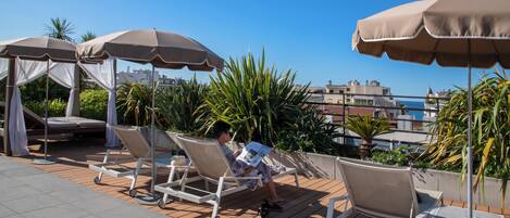 A rooftop lounge area with sun loungers, umbrellas, and a view of the cityscape.