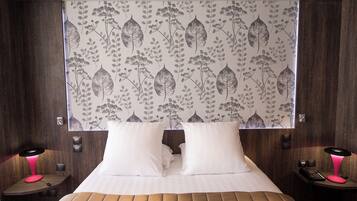 A hotel room with a large bed, two bedside tables, a nightstand, a window with a leaf-patterned curtain, and a wall-mounted telephone.