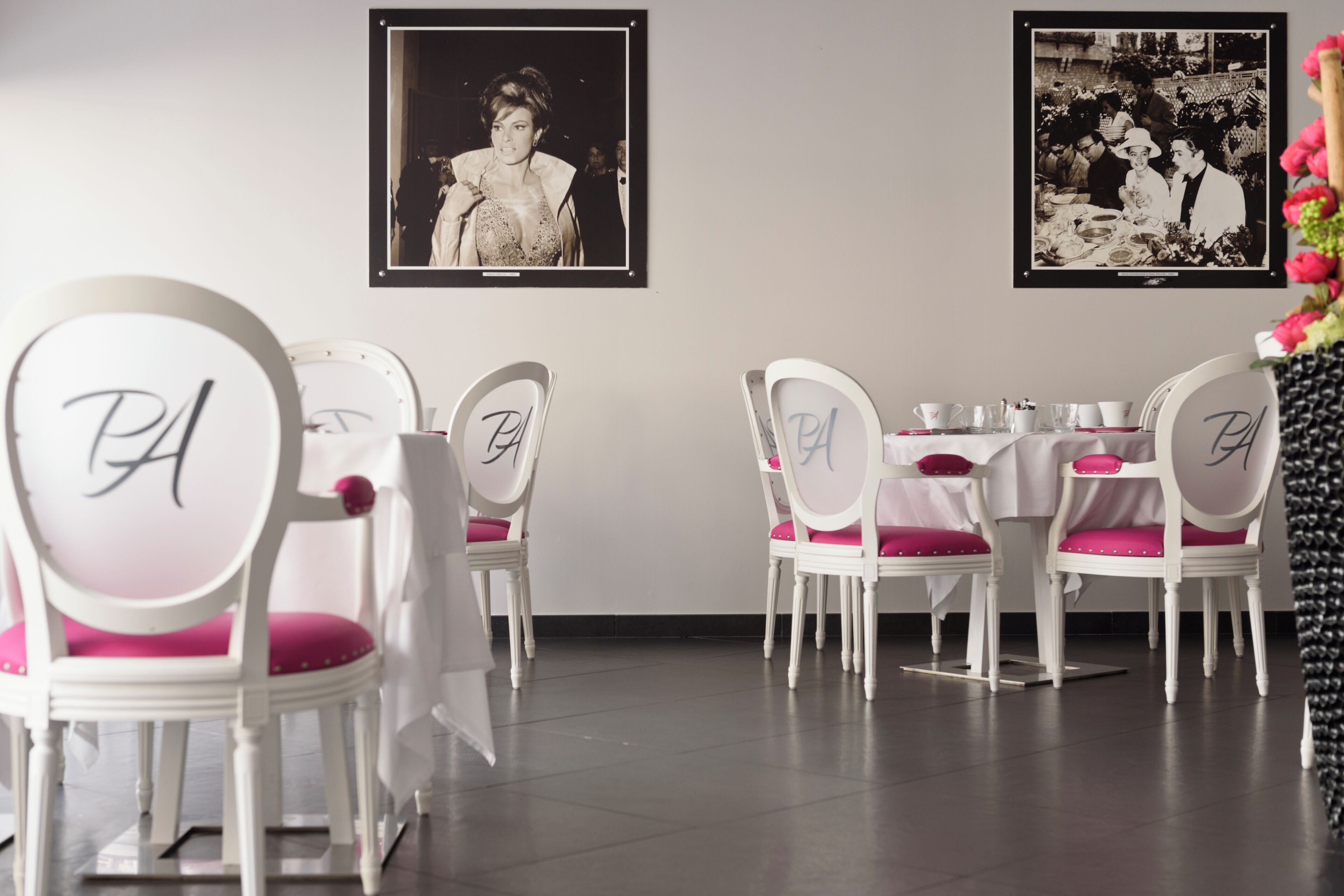 Un comedor con sillas y mesas blancas, cada una con un monograma 'PA' en el respaldo.