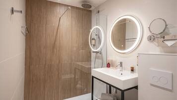 Un baño moderno con cabina de ducha de madera, puerta de vidrio para la ducha, lavamanos blanco con espejo y un perchero para toallas.