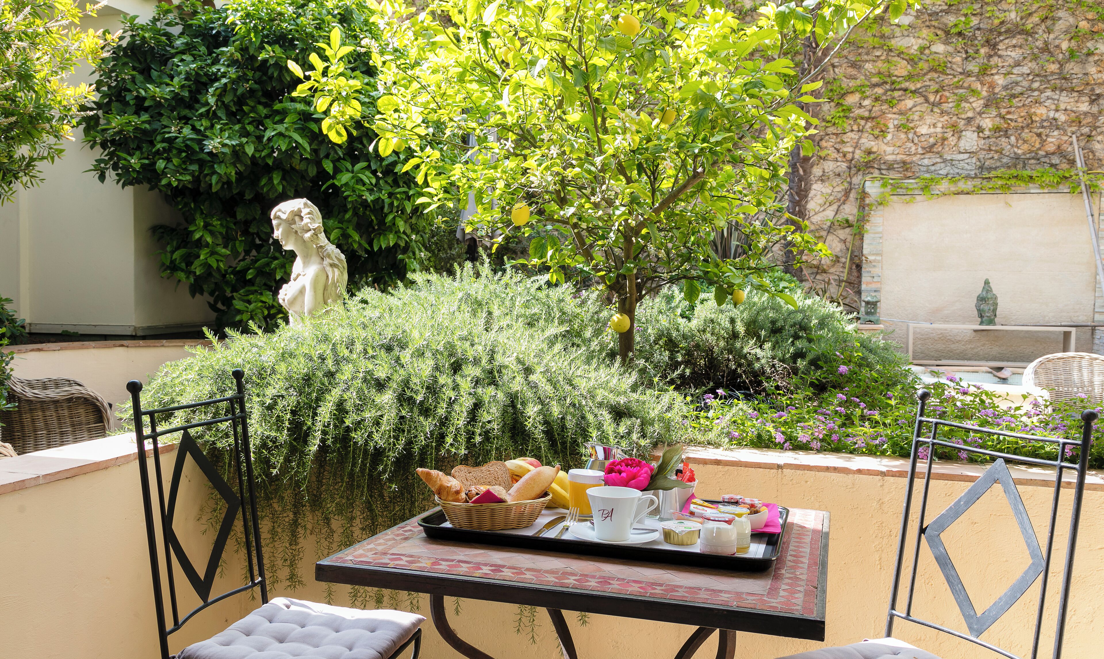 Zona exterior con mesas dispuestas para el desayuno, rodeada de vegetación y una estatua.