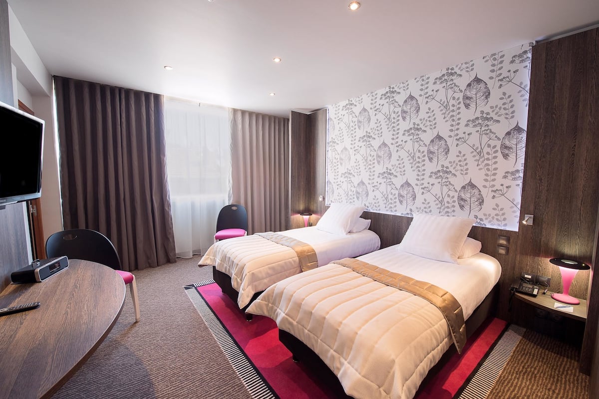 A hotel room with two beds, a TV, a desk, and a chair.