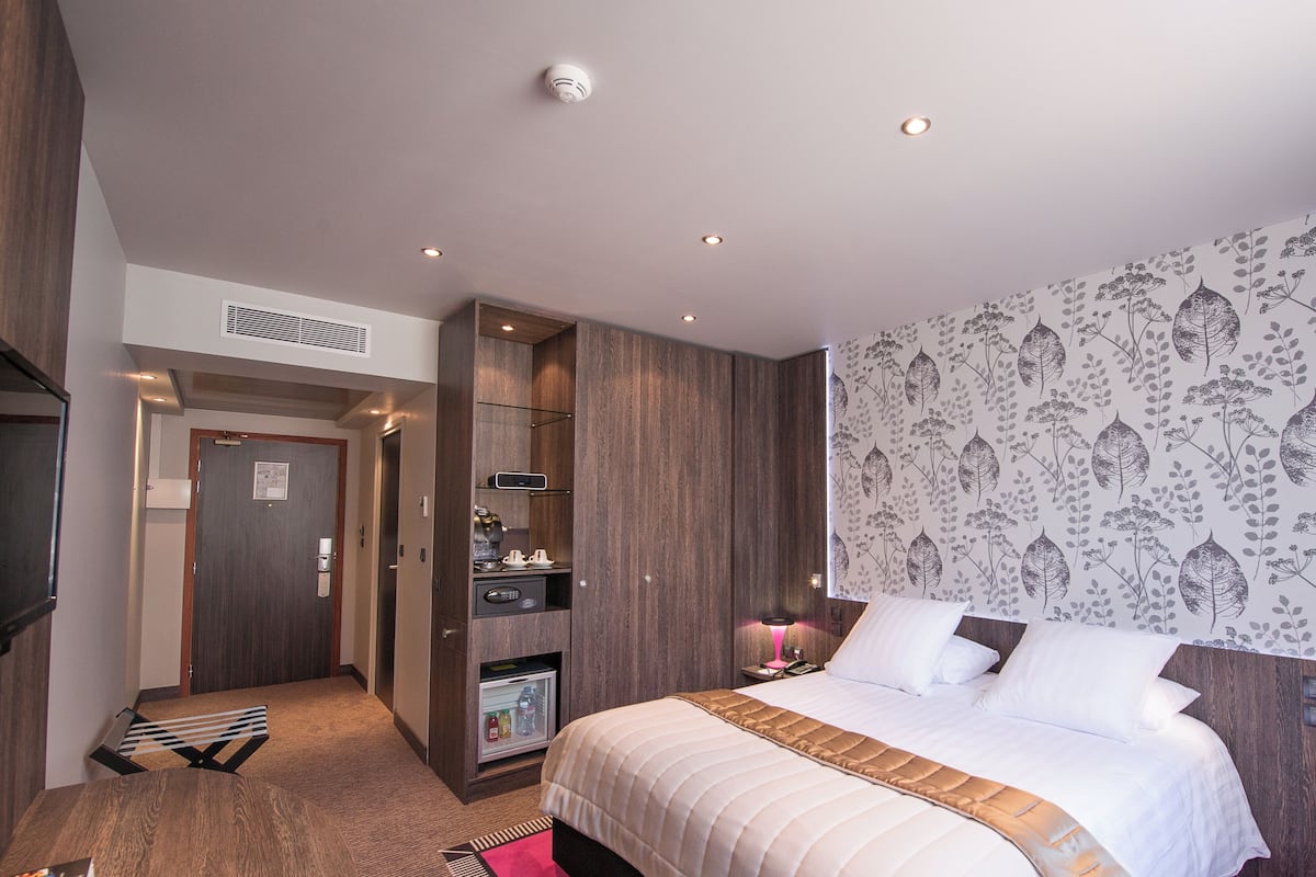 A modern hotel room with a large bed, a built-in wardrobe, a kitchenette, and a shower area.