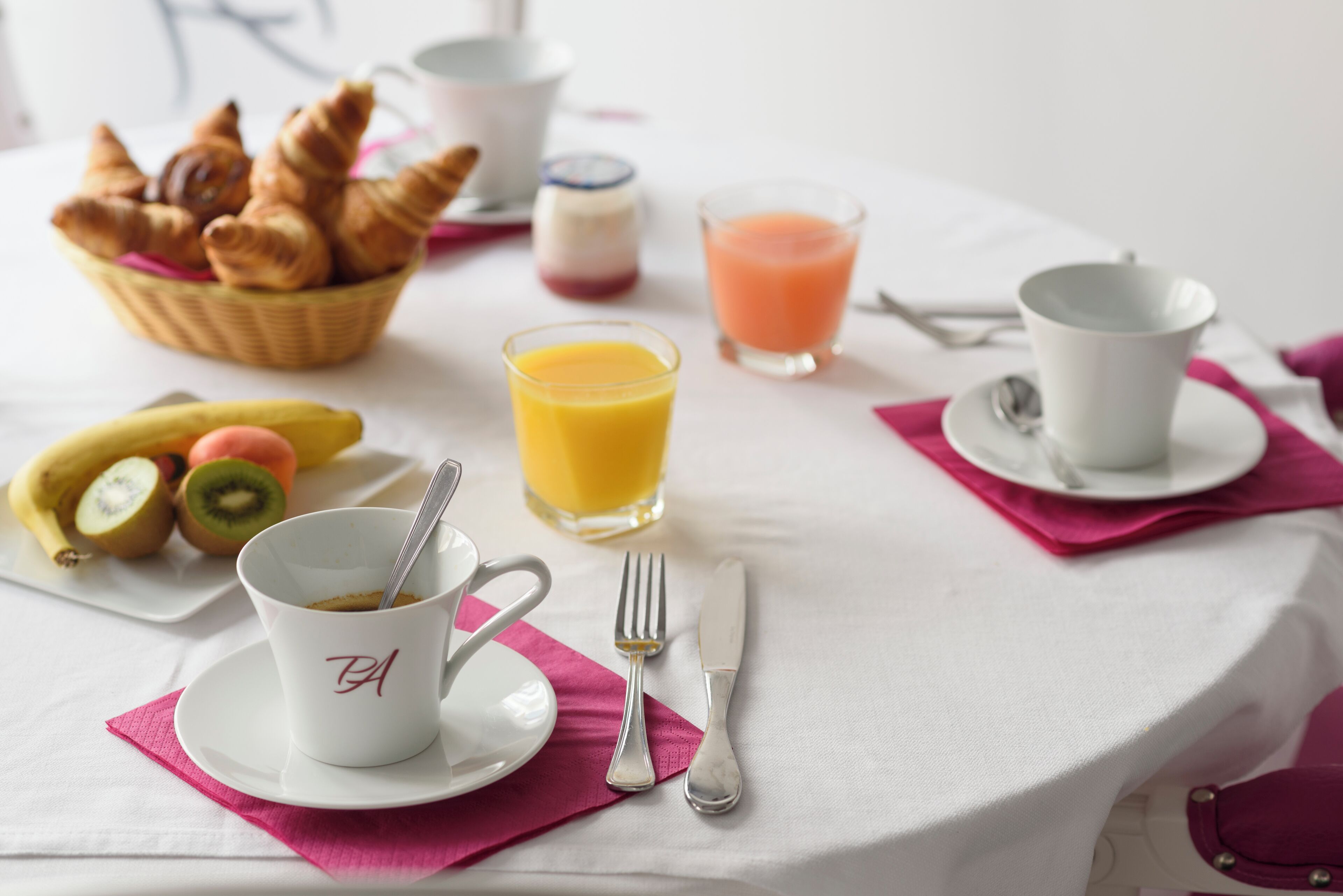 A breakfast table with croissants, fruit, and beverages.