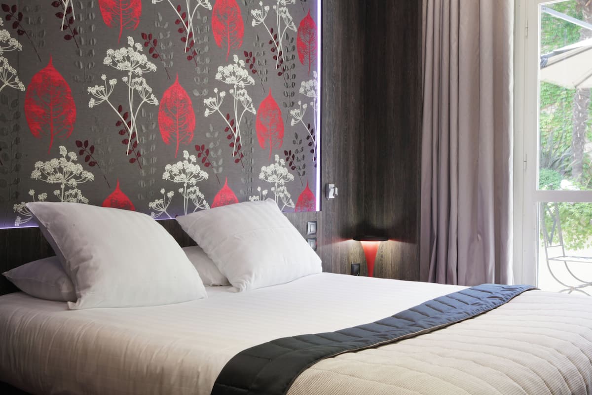 A neatly made bed with white and black bedding, a patterned wall behind it, and a window with curtains.