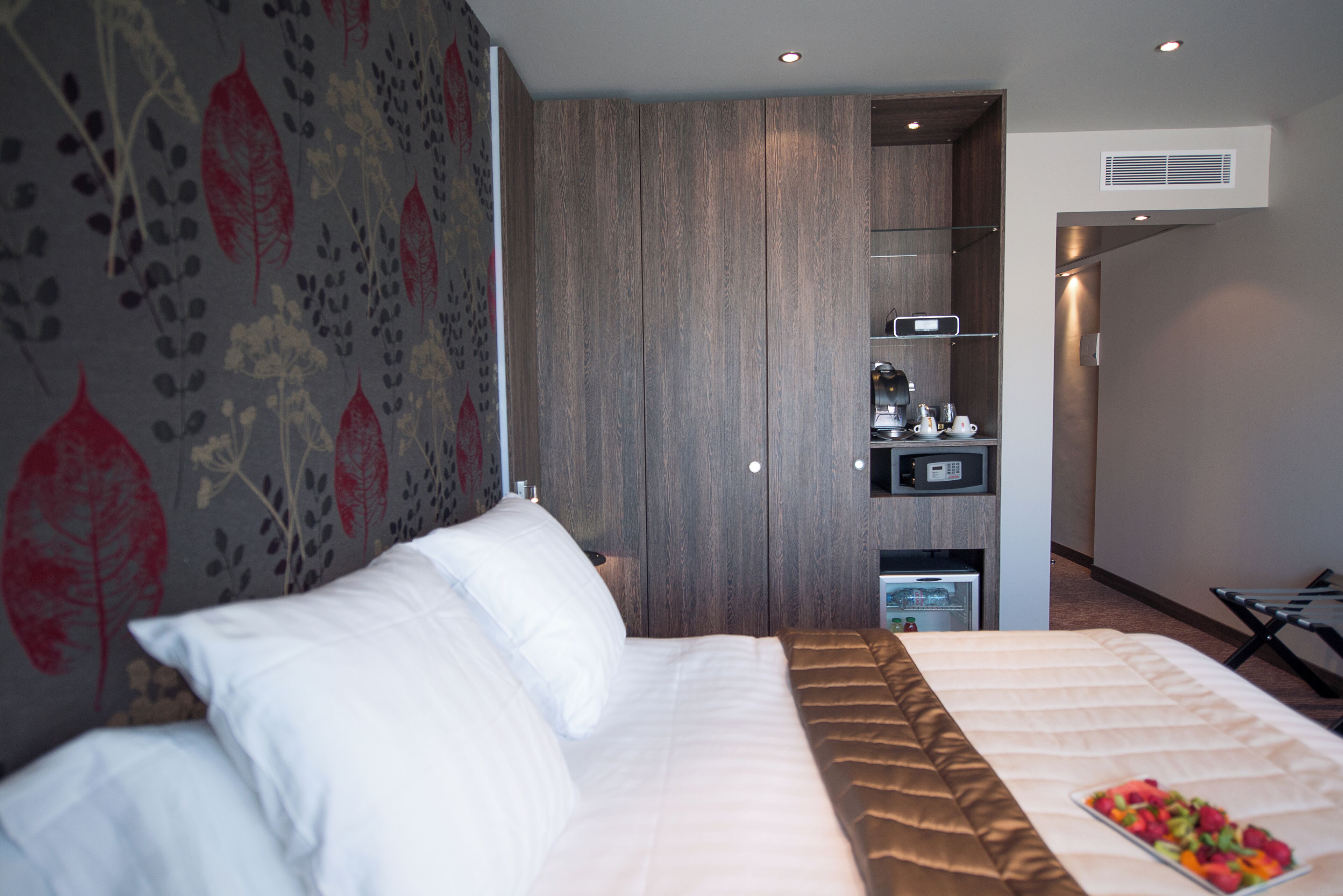 Habitació d'hotel moderna amb un llit gran, un armari encastat, un mini-frigorífic i una cuineta petita.