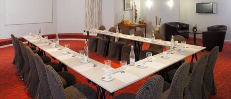 A conference room with a long table, chairs, a projector screen, and a television.