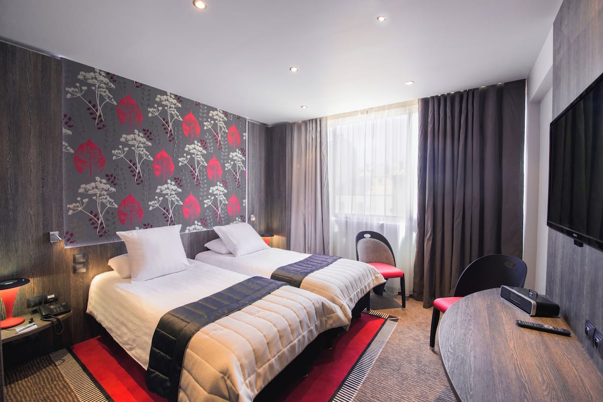 A hotel room with two beds, a desk, a chair, a TV, and a window with curtains.