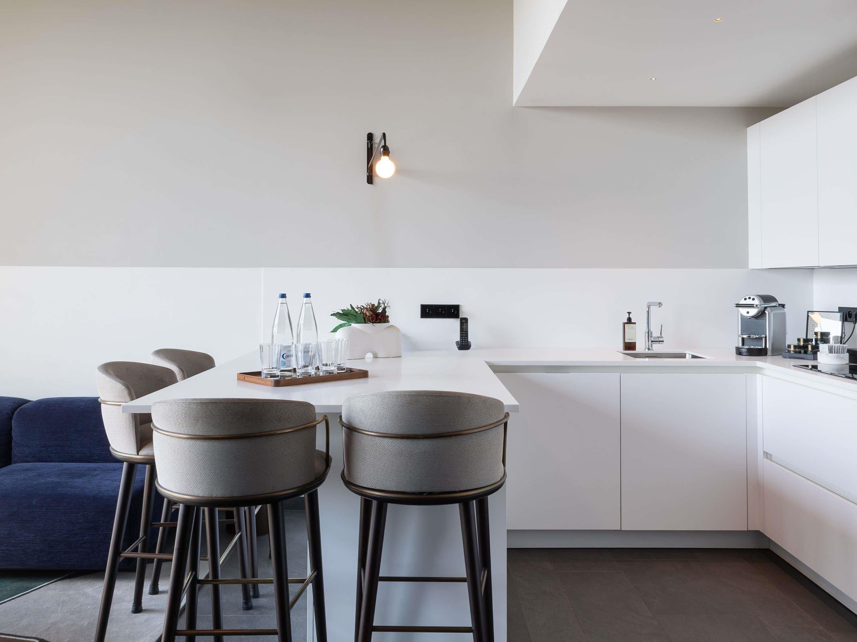 Una cocina moderna con una isla central, taburetes de bar, un sofá y una cafetera.