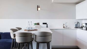 Una cocina moderna con una isla central, taburetes de bar, un sofá y una cafetera.