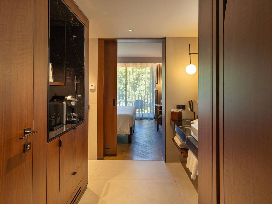 Habitació d'hotel amb armari de fusta, tocador de marbre, un llit i un balcó amb vistes a arbres.