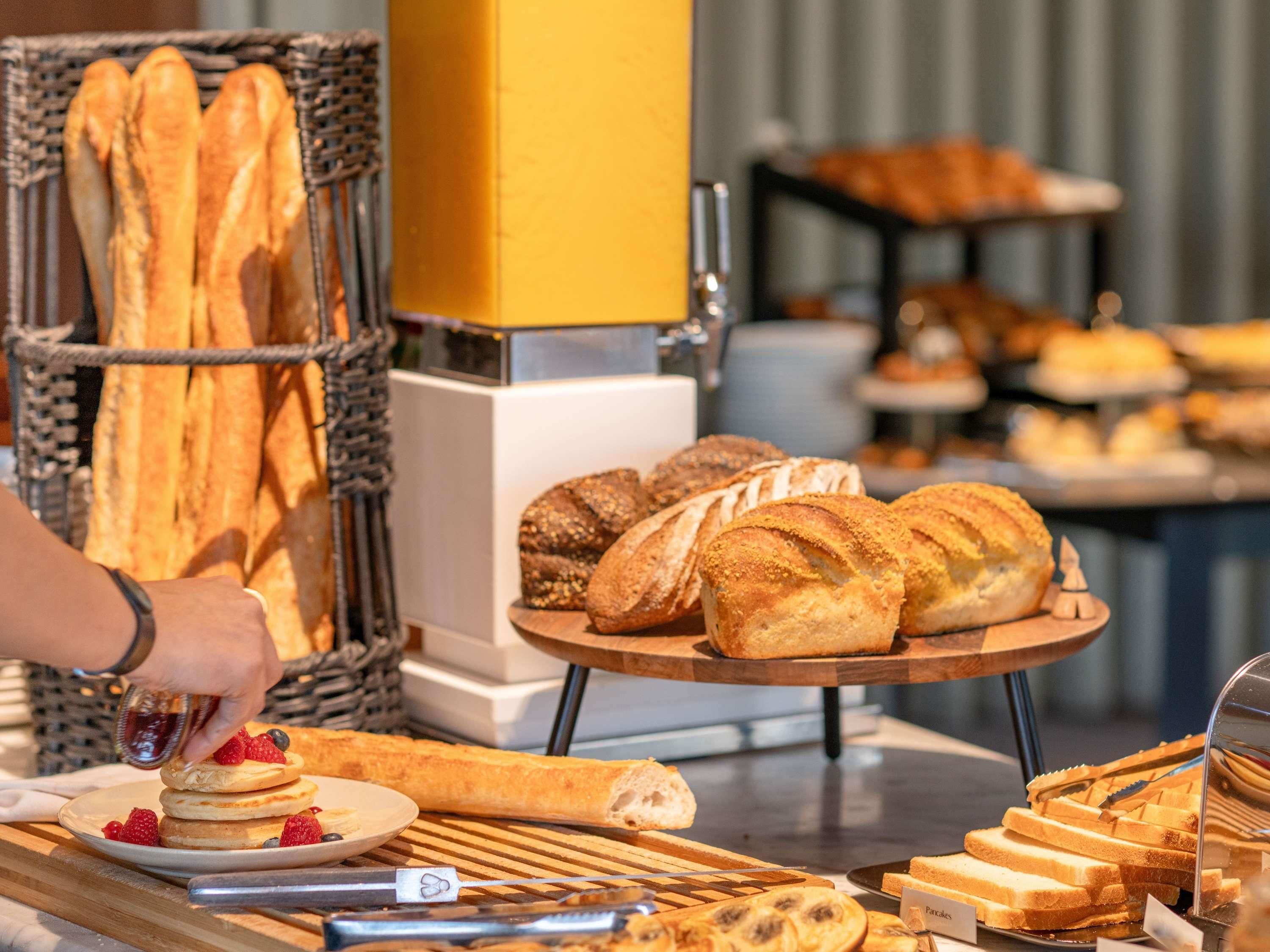 Un bufé de desayuno con panes, pasteles y una persona atendiendo.