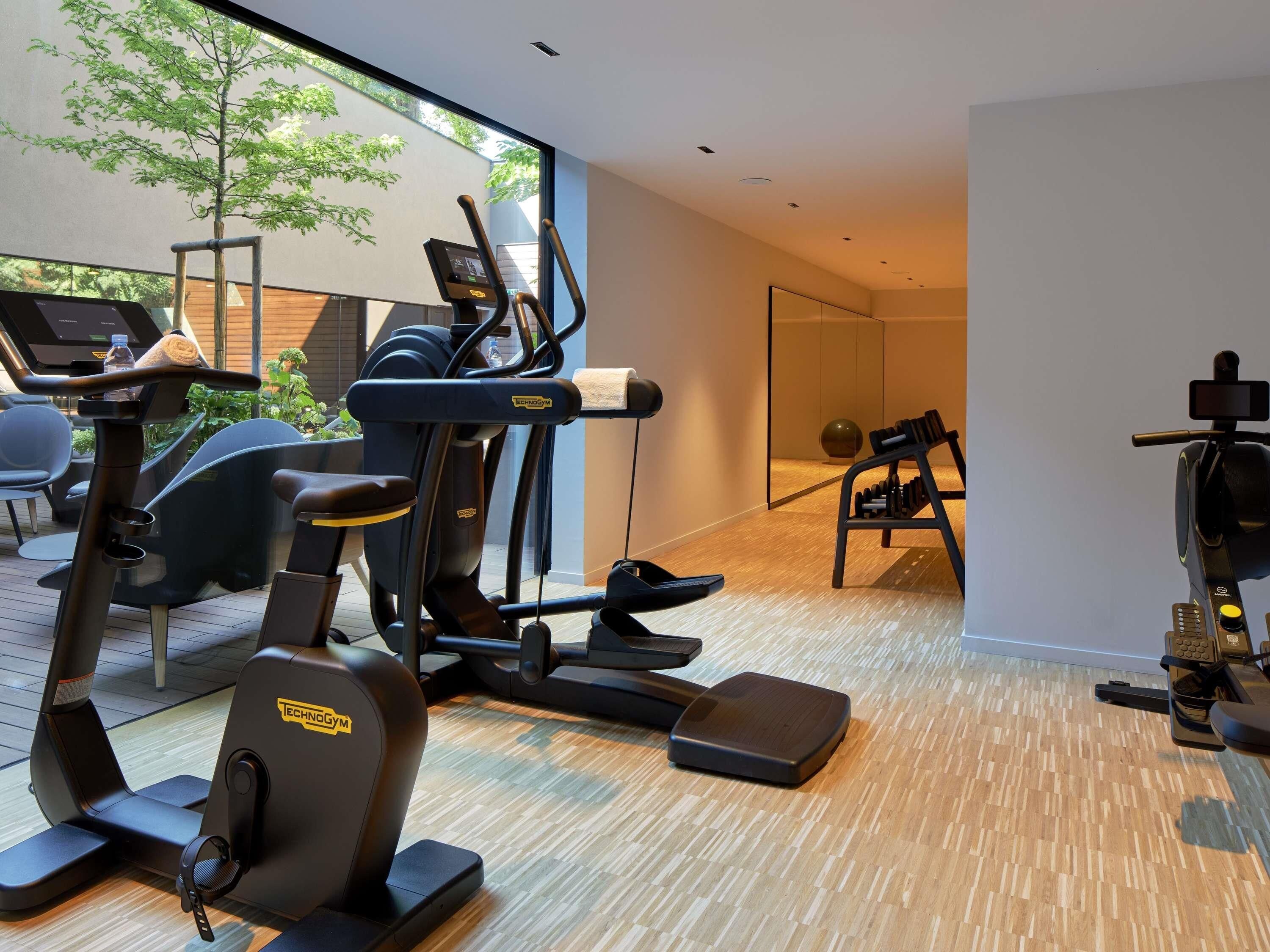 Ein modernes Fitnessstudio mit unterschiedlichen Trainingsgeräten, einem großen Fenster mit Blick auf Grünflächen und einem Holzboden.