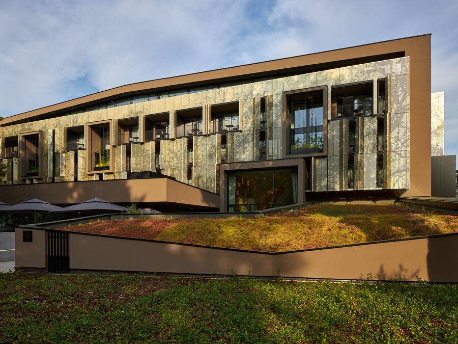 A modern building with a curved facade, multiple balconies, and a landscaped garden area.