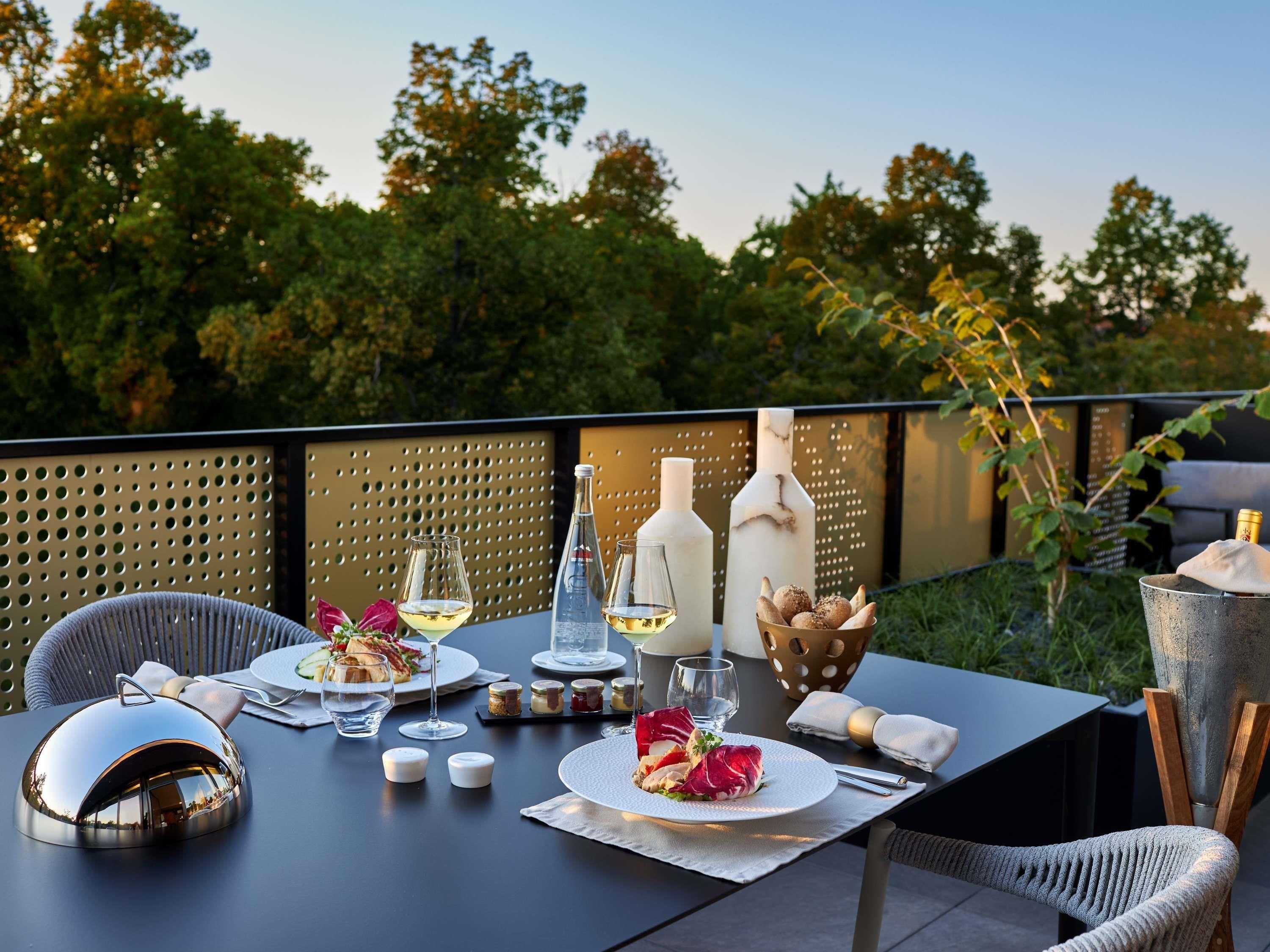 An outdoor dining setup with a table, chairs, wine glasses, bottles, and a decorative centerpiece.