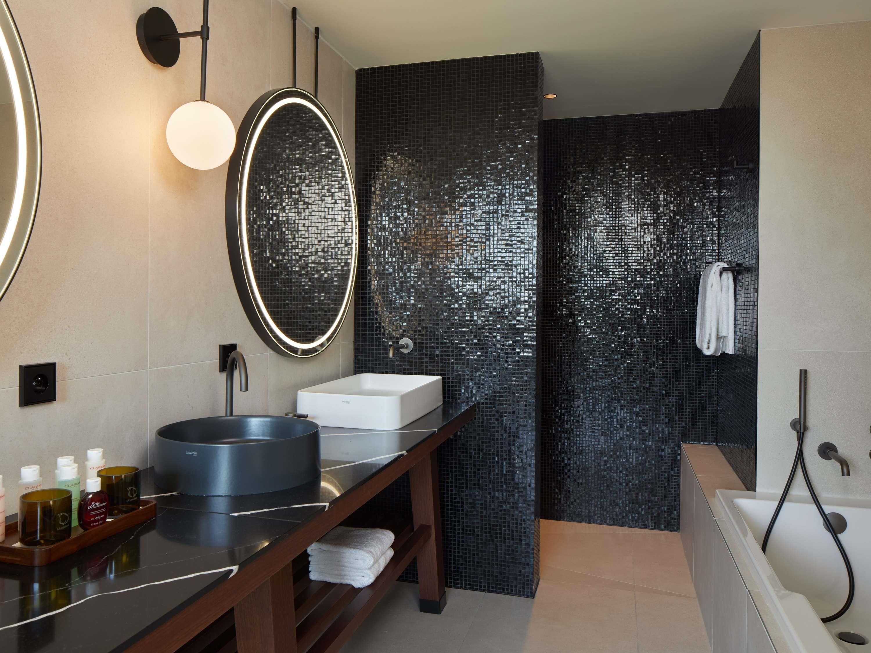 A modern bathroom with a round mirror, a rectangular sink, a bathtub, and a shower area.