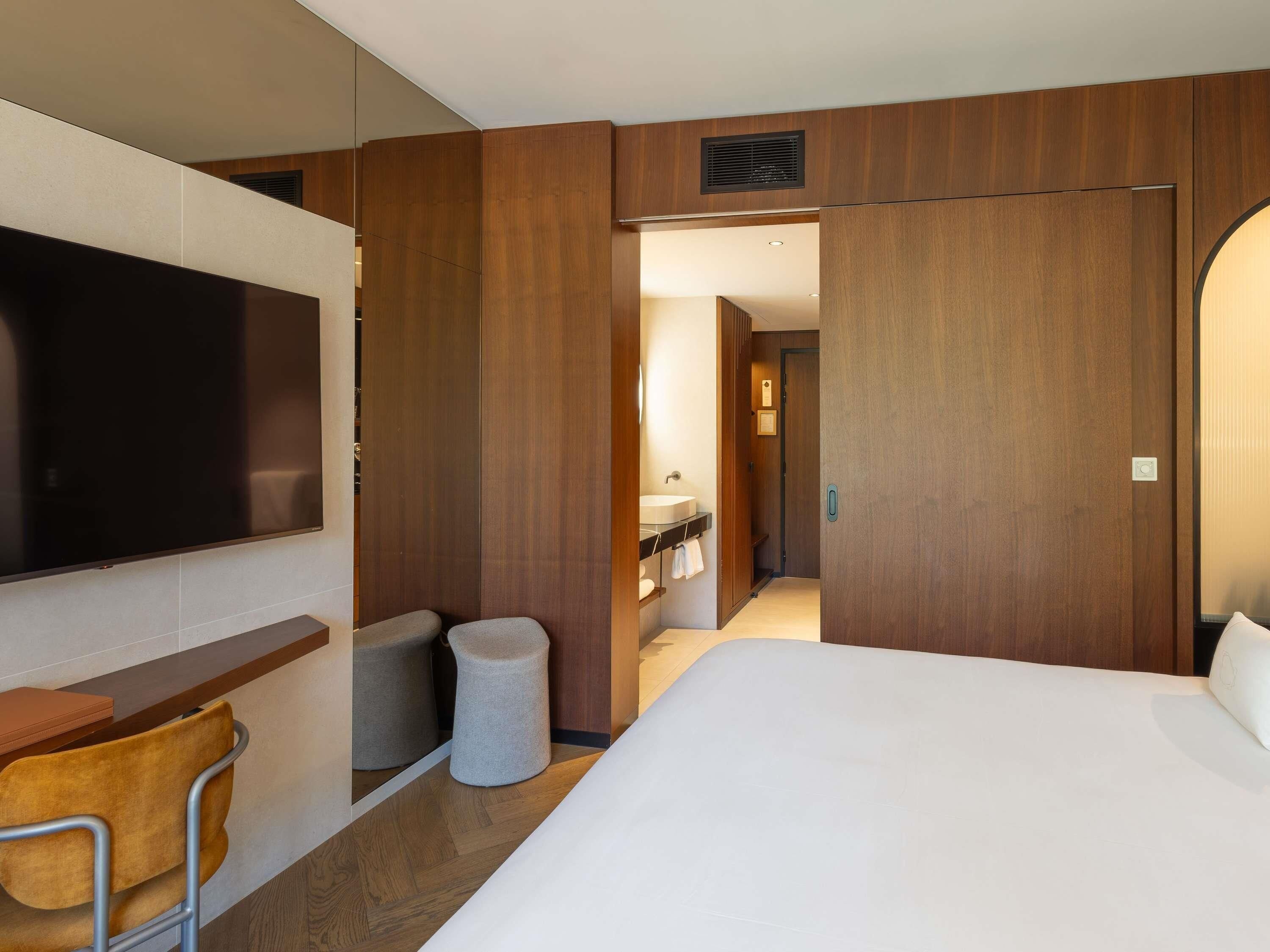 Una habitación de hotel con una cama, televisión, escritorio y baño visible a través de una puerta abierta.