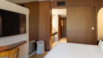Una habitación de hotel con una cama, televisión, escritorio y baño visible a través de una puerta abierta.