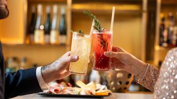 Dos personas brindando con bebidas en un bar, un menú y una barra con un logotipo.