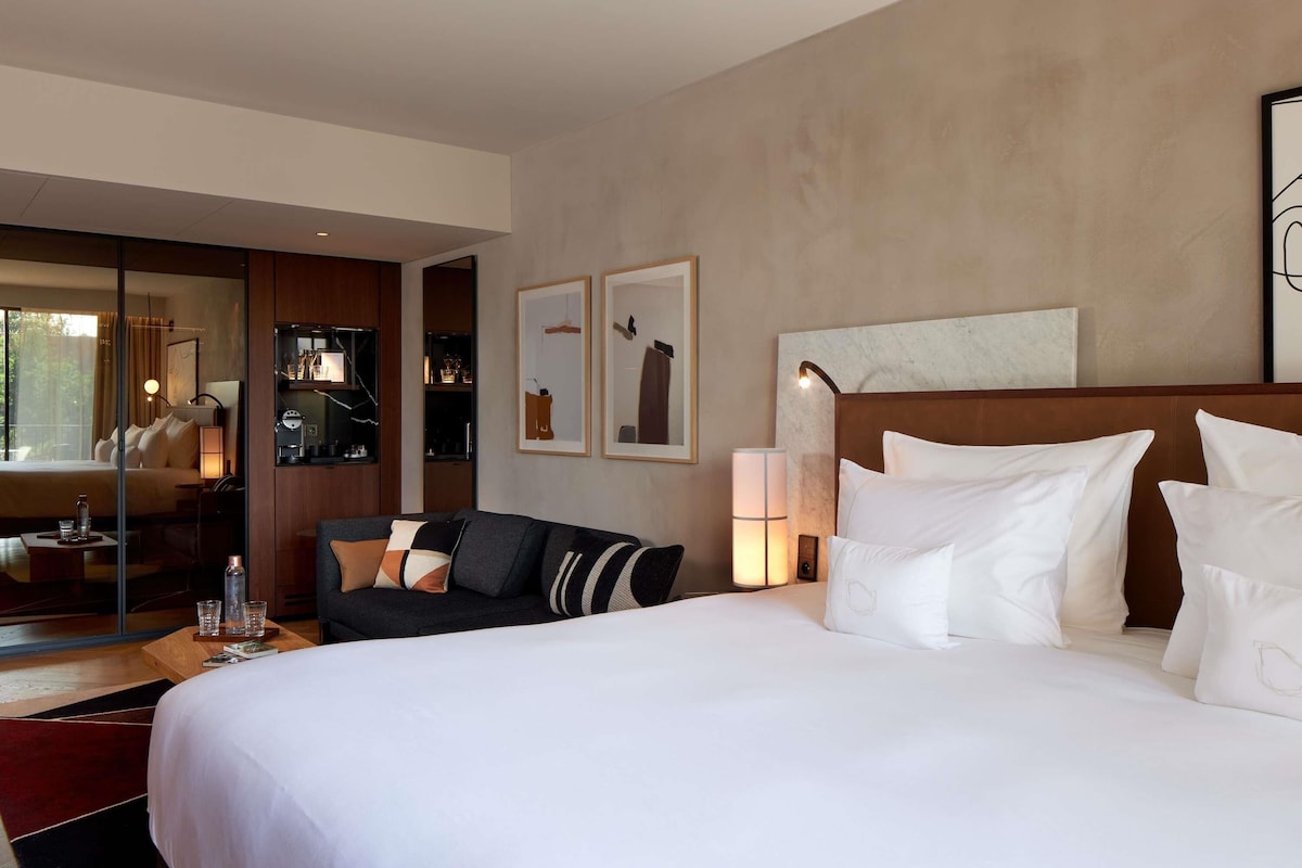 Une chambre d’hôtel avec un grand lit, un canapé, une table de chevet, un miroir et des œuvres d’art accrochées au mur.