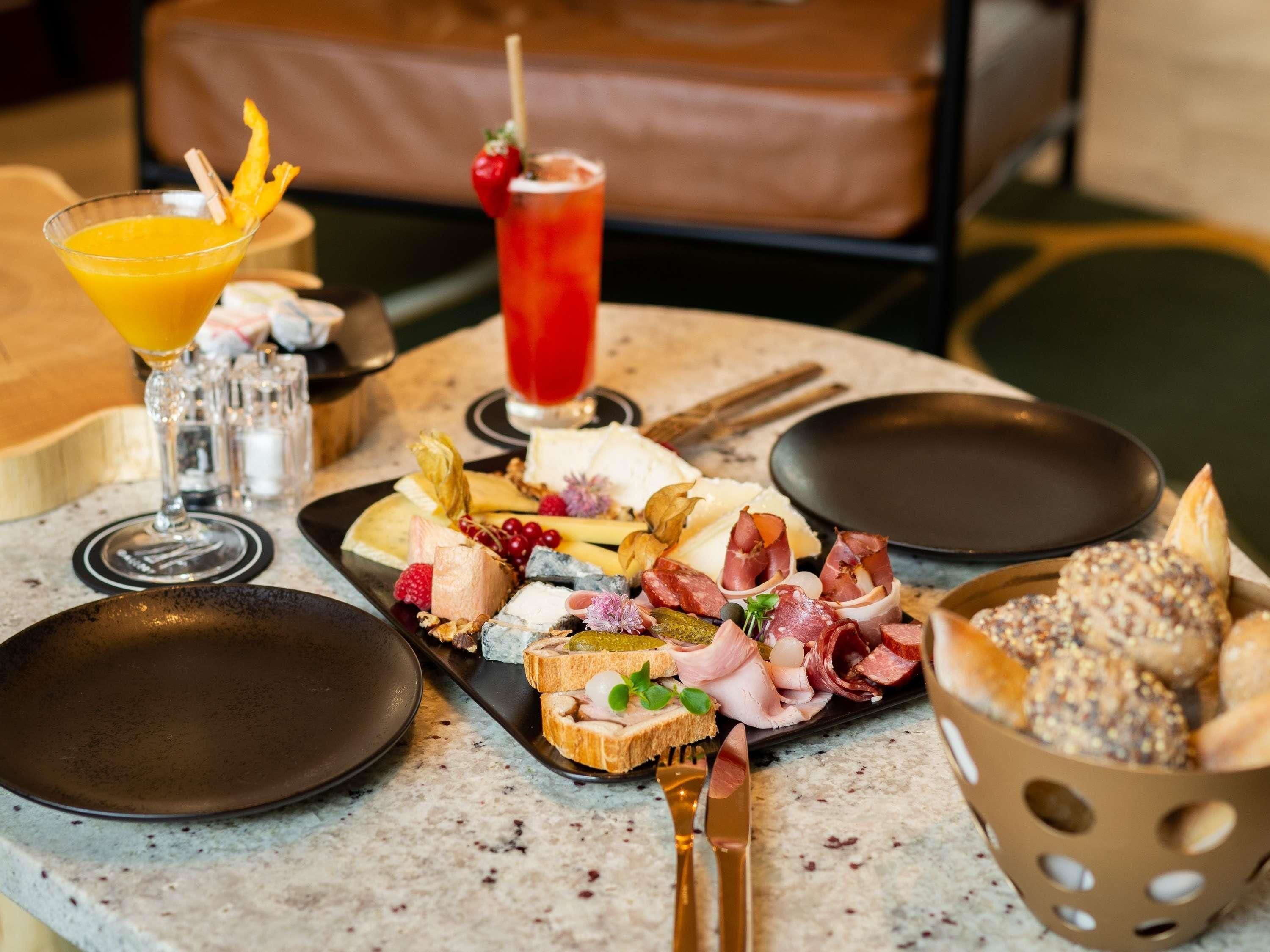Ein Tisch mit verschiedenen Speisen, darunter Käse, Fleisch und Brot, sowie zwei Getränke.