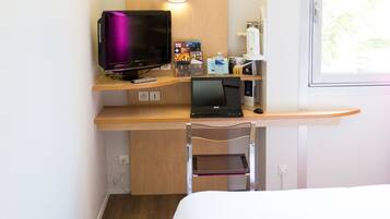 Une chambre d’hôtel avec un lit, un bureau avec un ordinateur portable, une télévision et une fenêtre.