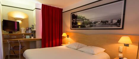 Una habitación de hotel con cama, escritorio con computadora, silla, televisor y un cuadro en la pared.