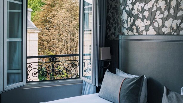 A hotel room with a large bed, a window with a view of trees, and a patterned wall. - Timhotel Paris Gare de l'Est (Paris)