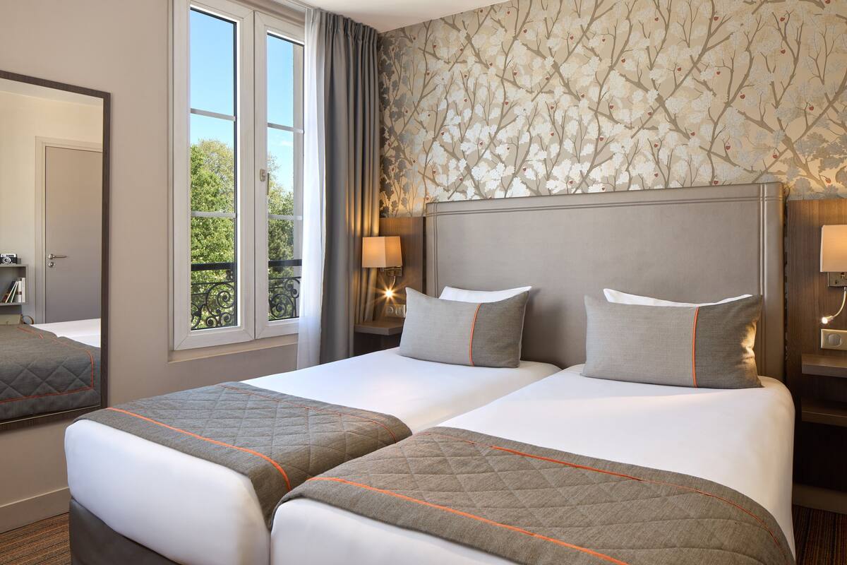 A hotel room with two beds, a large window, and a mirror.