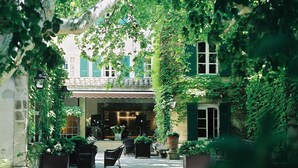 A courtyard with outdoor seating, potted plants, and a building with green shutters. - Le Prieure - Relais & Chateaux (Villeneuve-les-Avignon)