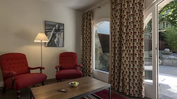 A room with two red armchairs, a wooden coffee table with a bowl and remote, a lamp, and a large window with floral curtains.