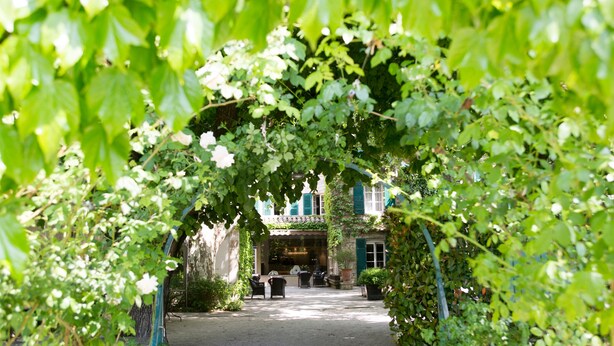 An outdoor seating area with tables and chairs under a green archway. - Le Prieure - Relais & Chateaux (Villeneuve-les-Avignon)