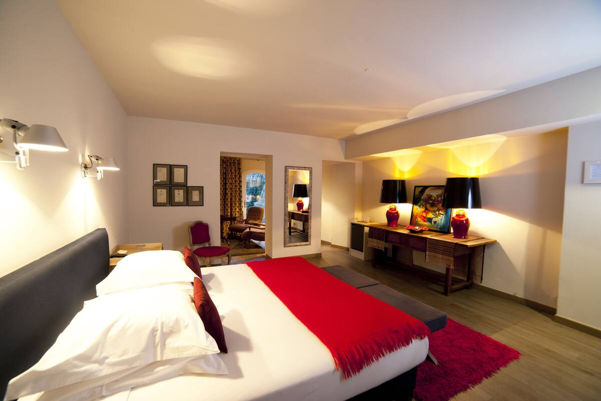 A hotel room with a large bed, a desk with a chair, a mirror, and wall-mounted lamps.