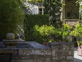 A stone wall with a stone balustrade, a potted plant, and a building with a window in the background.