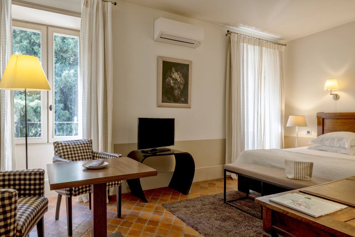 A hotel room with a bed, a desk with a chair, a television, and a window with curtains.