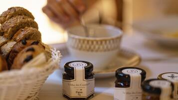 A table with a basket of sliced bread, a bowl, and small jars labeled 'Le Mas des Conifères'.