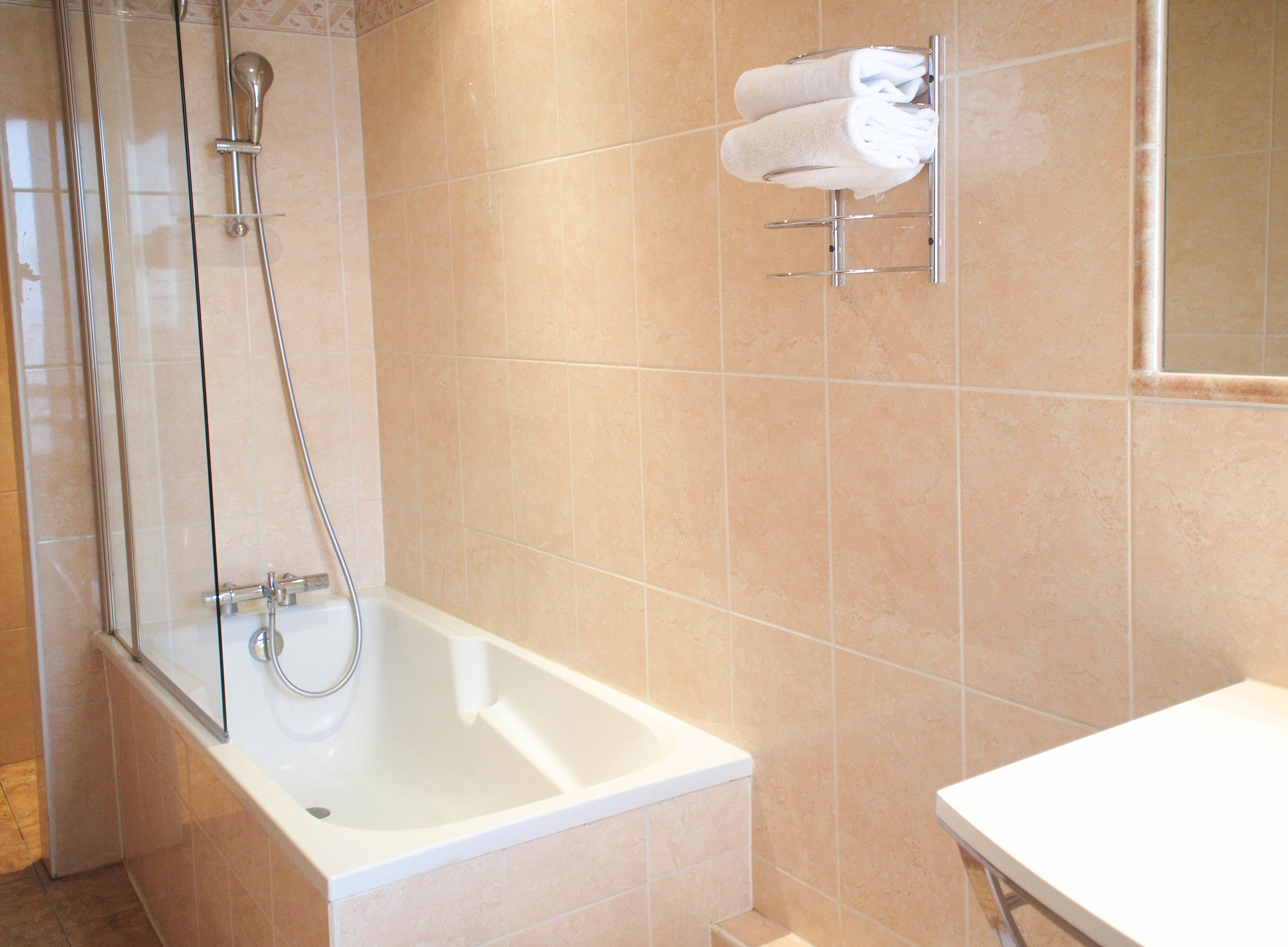 A bathroom with a glass-enclosed shower, a white bathtub, and a towel rack with two white towels.