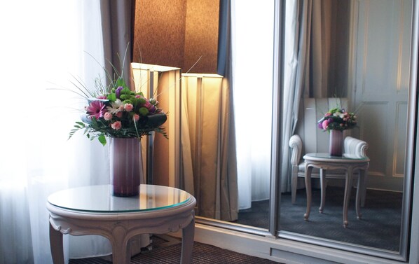A room with a glass table, a vase of flowers, a lamp, and a chair.