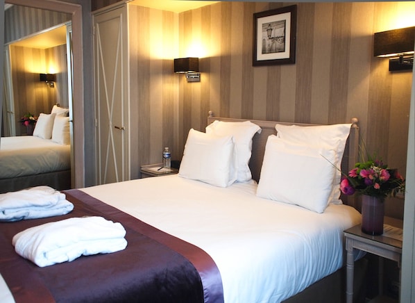 A hotel room with a large bed, a bedside table with a lamp, a mirror, and a picture on the wall.