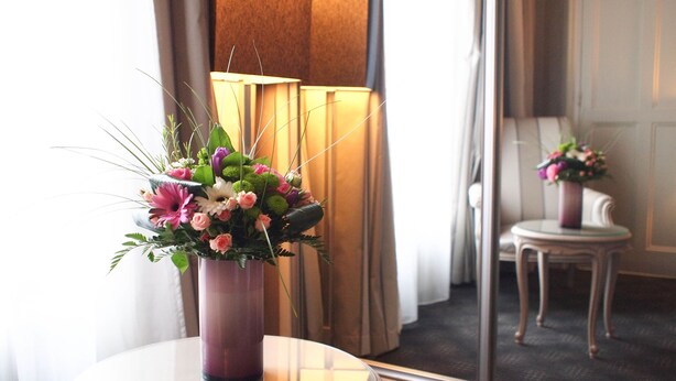 A room with a round glass table holding a purple vase with a floral arrangement.