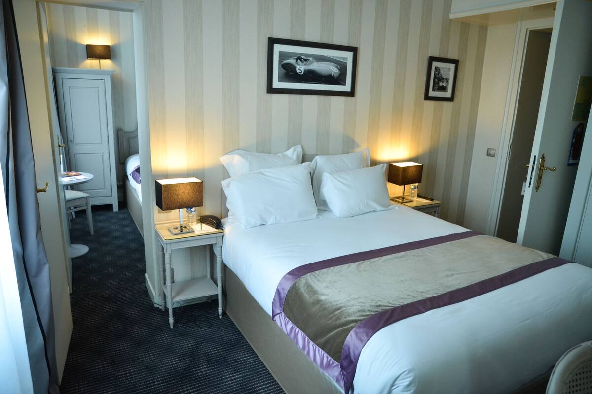Una habitación de hotel con cama, mesitas de noche, escritorio, silla y una pequeña mesa con lámpara.