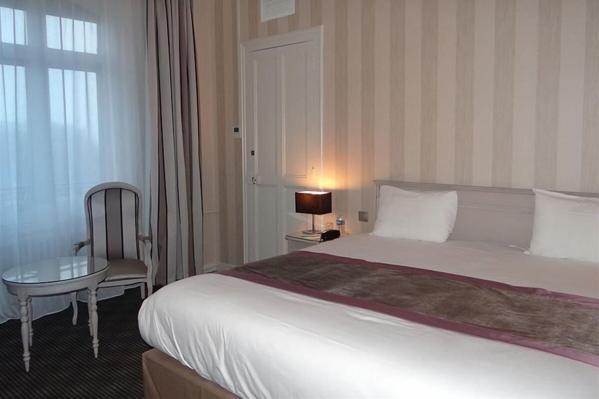 Habitación de hotel con una cama, una silla, una mesita de noche con lámpara y una puerta.
