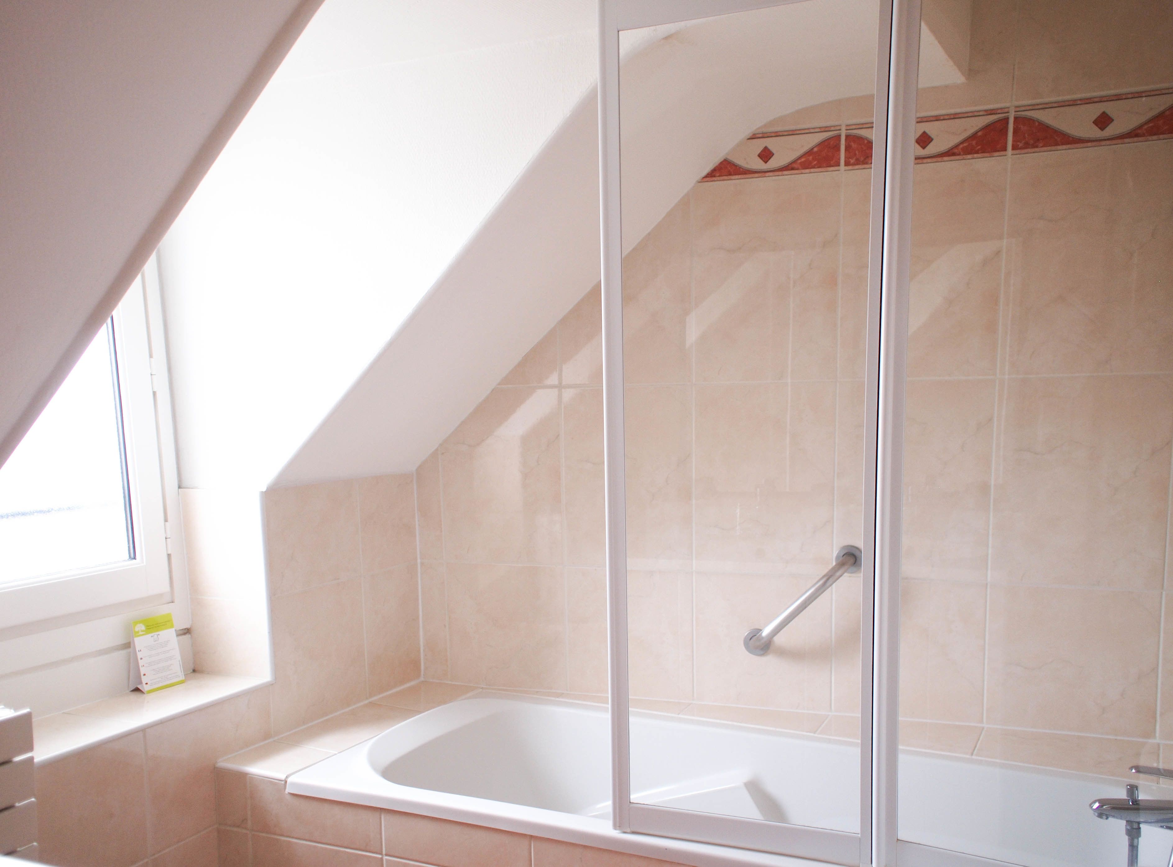 Un baño con bañera, mampara de cristal y ventana.