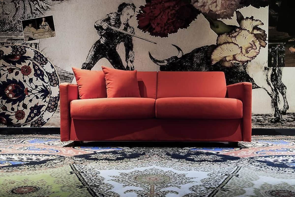 A red sofa in a room with a patterned carpet and a large decorative wall.